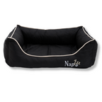 Napzzz divan hondenmand in zwart in vooraanzicht. Mand is zeer stevig gevuld in de opstaande randen en voorzien van een uitneembaar ligkussen met schuimrubber matras als vulling. Mand en ligkussen zijn beide voorzien van ritssluiting. De randen zijn verhoogd en voorzien van aparte binnenhoezen, zodat de buitenhoes eventueel gewassen of gelucht kan worden. De stof is oxford dus waterafstotend en is mooi afgewerkt en geborduurde Napzzz logo. Luxe en comfortabel en in meerder maten verkrijgbaar