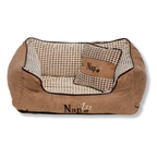 NapZZZ divan beige met kussen voor honden in vooraanzicht. De mand is zeer stevig gevuld in de opstaande randen voor extra steun en comfort. 
De buitenstof heeft een fluweel look en de binnenzijde is bekleed met blokjes relief. Tevens voorzien van en afneembaar kussentje. Het liggedeelte is voorzien van een uitneembaar en omkeerbaar ligmatras. De ene kant is voorzien van blokjes relief en de andere zijde is voorzien van effen bruine stof zoals de buitenzijde. Mand voorzien van ritssluiting aan binnenzijde.